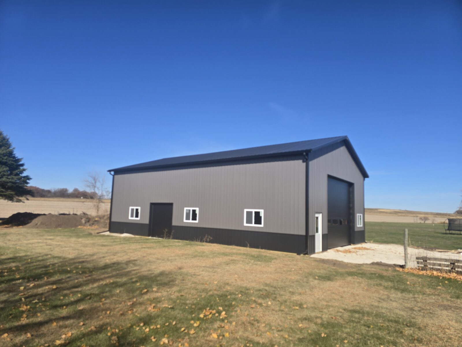 Side angle view of 36x56x16 insulated post frame shop with charcoal steel siding and black wainscot in Millington Illinois